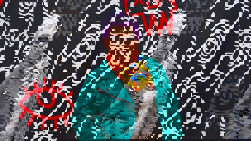 Kvinna i färgstarka kläder och lila hår. 