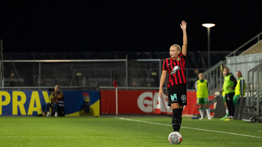 Kvinna på fotbollsplan, iklädd svart-röda kläder och stäcker upp ena armen.